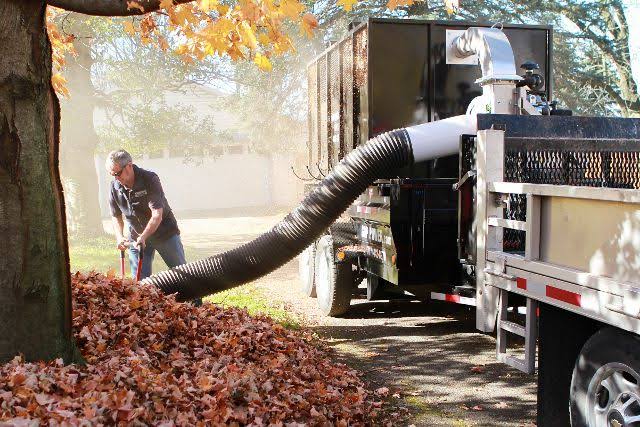Truck-mounted leaf vacuum clearing a fall property
